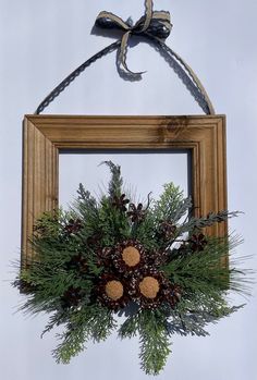 a wooden frame hanging on the wall with pine cones and evergreens in it, tied to a rope