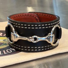 Revitalization of a Rebecca Ray Classic, this premium bridle leather Snaffle Bit Cuff bracelet is benchmade in America featuring a double contrast stitch all the way around and either stainless steel or brass hardware. A bold statement piece measuring 1 1/2" wide and 9 1/2" long and lined with a contrasting bridle leather color. This bracelet will only get better with time as the bridle leather breaks in. They are just stunning! Each bracelet has two sizing holes that measure 7 1/4" and 7 3/4" f Classic Leather Cuff Bracelet, Classic Leather Bracelet With Black Band, Leather Cuff Bracelets With Custom Hardware, Used Saddles, Snaffle Bit, Orange Bracelet, Horse Jewelry, Leather Conditioner, Leather Cuffs