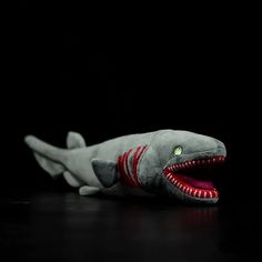 a stuffed shark with its mouth open and teeth wide open, on a black background