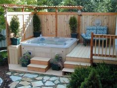 a hot tub sitting in the middle of a garden next to a wooden fence and steps