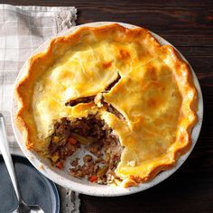 a meat pie is cut in half on a plate next to a fork and spoon