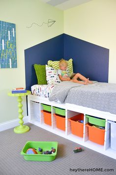 a young boy laying on top of a bed next to toy bins