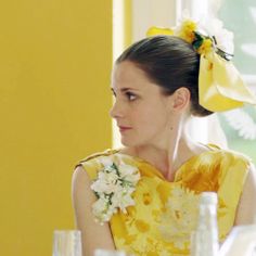 a woman sitting at a table with flowers in her hair and wearing a yellow dress