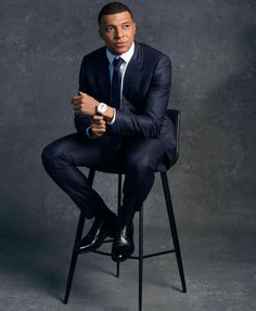 a man in a suit and tie sitting on a chair with his arms folded up