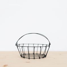 a wire basket sitting on top of a wooden table next to a white wall in the background