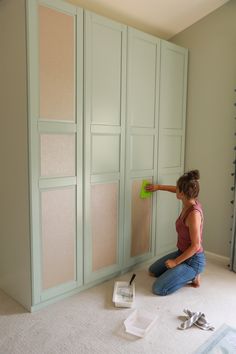 a woman sitting on the floor in front of some cupboards and paint rollers