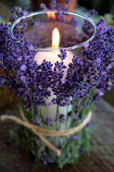 a glass vase filled with purple flowers and a lit candle