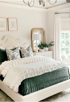 a white bed with green comforter and pillows in a bedroom next to a window