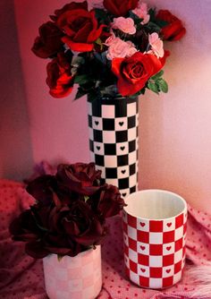 two vases with roses in them sitting on a red and white checkered table cloth