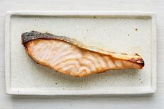 a piece of fish that is on a white plate with some brown stuff in it