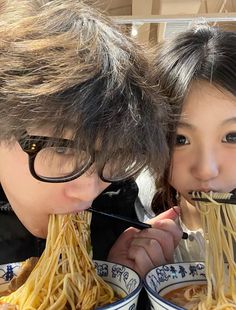 two people eating noodles with chopsticks in their mouths