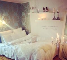 a white bed sitting in a bedroom next to a wall with candles on top of it