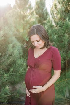 a pregnant woman standing in front of pine trees with her belly tucked under her stomach