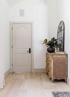 a white room with a wooden dresser and mirror on the wall, next to a door