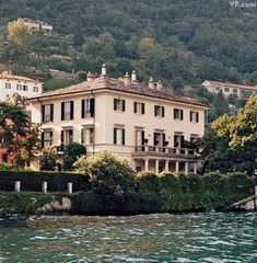 a large white house sitting on top of a lush green hillside next to a body of water