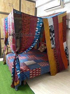 a bed covered in many different colored pieces of cloth on top of green carpeted flooring