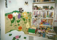 a book shelf filled with lots of books next to a wall covered in cartoon art