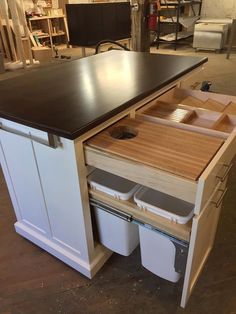 a kitchen island with two bins and an open drawer on the bottom that holds trash cans