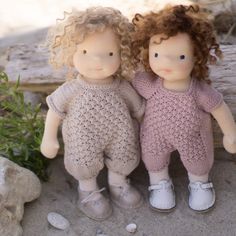 two dolls are sitting next to each other on the ground near some rocks and plants