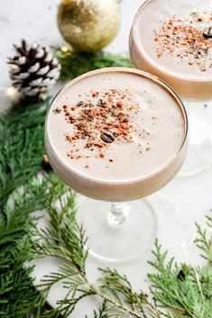 two glasses filled with drink sitting on top of a table next to pine cones and christmas decorations