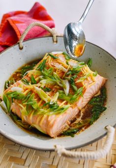 a fish dish is being served in a bowl with a spoon on the side and a pink towel next to it