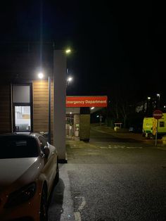 two cars are parked in front of a gas station at night with the lights on