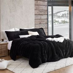 a bed with black and white comforters in a bedroom next to a window overlooking the snow covered mountains