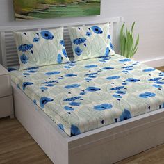 a bed with blue flowers on it in a room next to a painting and wooden floors