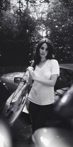 black and white photograph of a woman holding a surfboard in front of her car