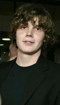 a young man with curly hair wearing a black suit