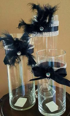 two clear vases with black feathers on them sitting on top of a wooden table