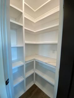 an empty pantry with white shelves and wood flooring in the corner, viewed from inside