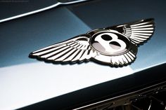 the number eight emblem is on the hood of a bentley car with wings flying around it