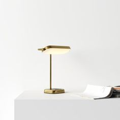 a desk lamp sitting on top of a white table next to a book and magazine