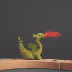 a small green toy sitting on top of a wooden table next to a red object