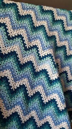 a blue and white crocheted blanket hanging on a wall next to a window