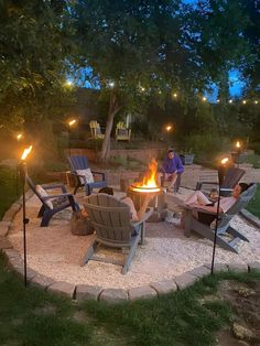 a fire pit surrounded by lawn chairs with candles lit in the middle and people sitting around it