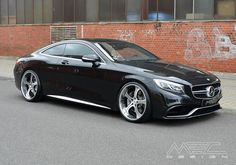 a black mercedes benz coupe parked in front of a brick building