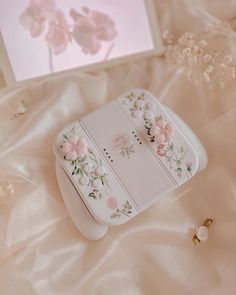 an electronic device with flowers on it sitting on a white blanket next to a flowered frame