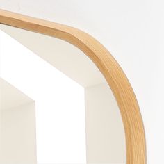 an arched wooden mirror hanging on the wall next to a white wall with light coming through it