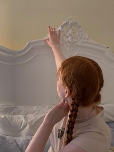 a woman with red hair is sitting on a bed and reaching up to the ceiling