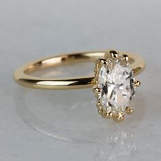 a yellow gold engagement ring with an oval cut diamond in the center, on a white surface