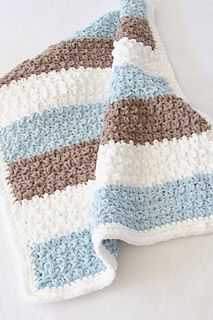 a crocheted blanket laying on top of a white tablecloth covered in blue and brown stripes