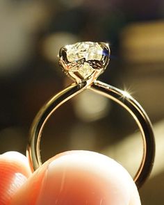 a close up of a person's hand holding a ring with a diamond on it