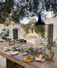 a wooden table topped with plates and bowls filled with food next to an olive tree