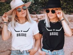 two women wearing matching shirts and hats standing next to each other in front of some rocks