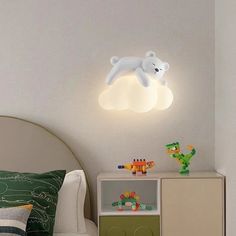 a white teddy bear sitting on top of a cloud shaped light above a child's bed