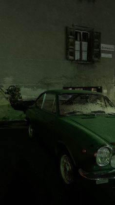 an old green car parked in front of a building at night with the lights on