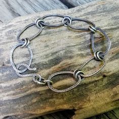 This silver chain bracelet was made with Argentium Silver square wire that was formed into oval shapes and textured on both sides. The organically shaped links were connected to each other with 2 jump rings made of Argentium Silver wire. The handcrafted hook is also Argentium Silver wire. The finished bracelet was oxidized to enhance the textured marks and then polished to reveal the silver. Oxidized Metal Bracelet With Oval Links, Oxidized Metal Chain Bracelet With Oval Links, Sterling Silver Bracelet With Oval Links, Handmade Metal Chain Bracelet With Rectangular Links, Handmade Chain Bracelet With Rectangular Metal Links, Silver Adjustable Chain Bracelet With Hook And Links, Adjustable Silver Chain Bracelet With Hook And Links, Adjustable Oval Link Sterling Silver Bracelet, Modern Nickel-free Oval Link Chain Bracelet