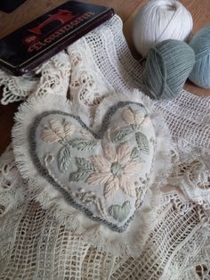 two balls of yarn and a heart shaped pillow on a lace tablecloth with crocheted doily